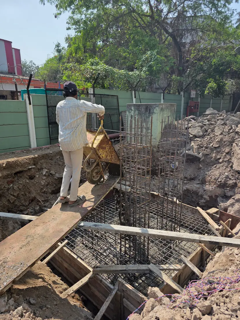 Site crew placing a wheelbarrow concrete pour beside a reinforced column footing cage