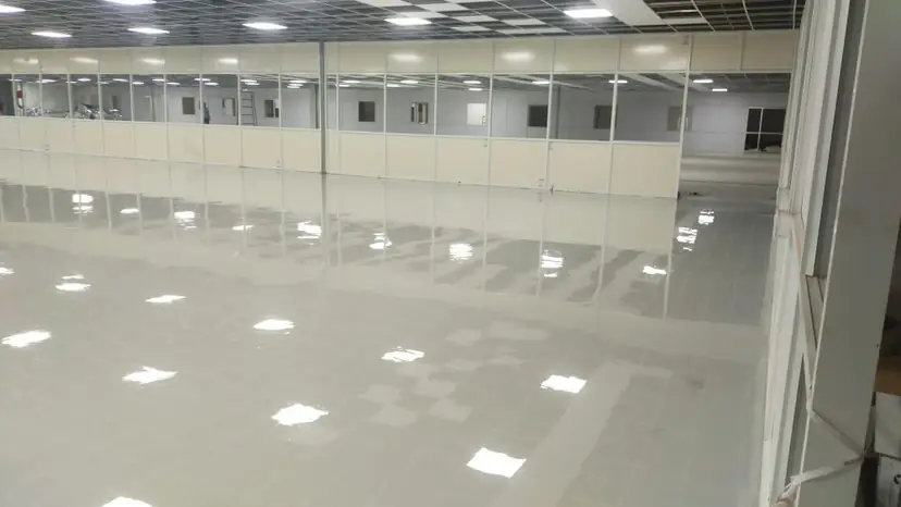 Freshly applied glossy epoxy floor coating across a large industrial hall with partition walls
