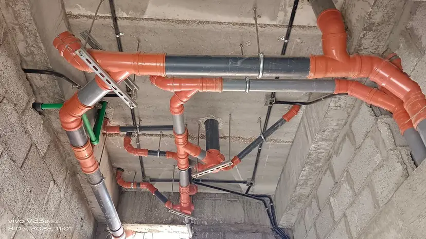 Overhead CPVC and cast-iron drainage pipe routing at a ceiling slab junction, mid-installation